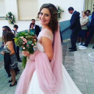 Novia sonriente con maquillaje natural y ramo de flores en su boda