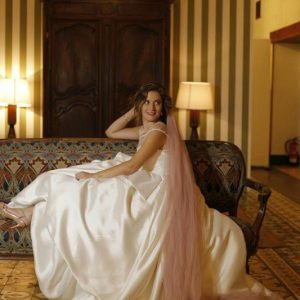 Novia sentada con vestido de satén y velo rosa en interior antes de la ceremonia